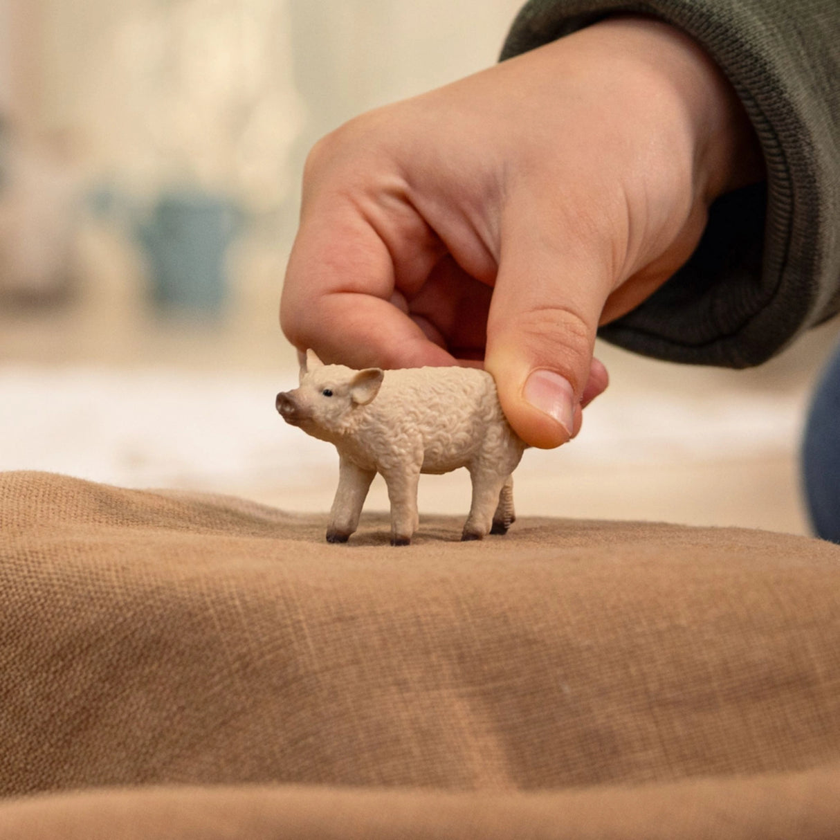 A child playing with a Schleich Mangalica Piglet farm animal toy inside a playroom