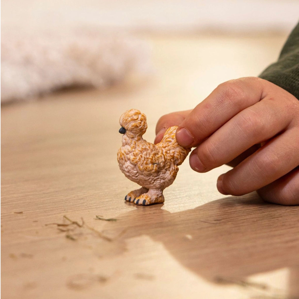 A child playing with Schleich Silkie Chicken Farm Animal Toy on a playroom floor