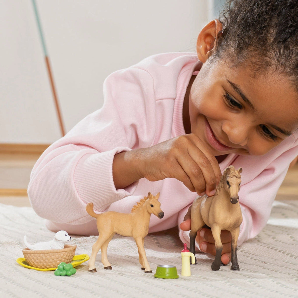 A child playing with the Schleich Horse Club Sarah's Baby Animal Care toy set inside a cozy playroom