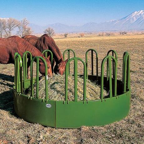 two horses stand side by side and eat hay from a large hay bale feeder