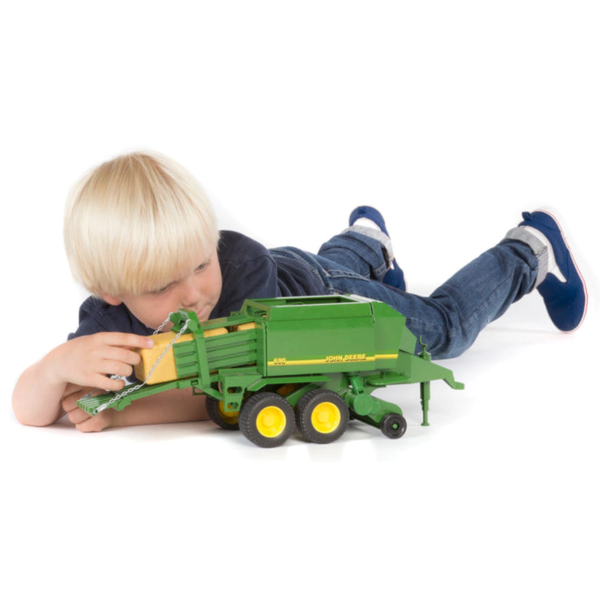 A kid playing indoors with the Bruder John Deere Toy Big Baler Press