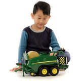 A Bruder John Deere toy round bale press being played by a kid indoors