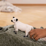 A child's hand playing with the Schleich Galloway Cow farm animal toy in a cozy playroom
